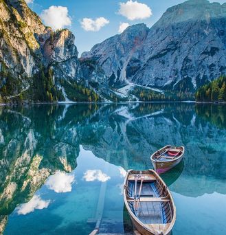 In einem spiegelglatten See spiegelt sich die atemberaubende Berglandschaft. Auf dem See befinden sich 2 kleine Ruderboote aus Holz.