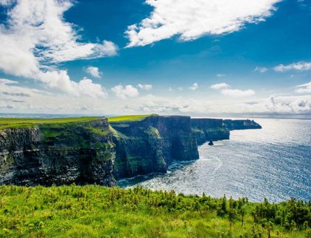 Eine steile Klippe ragt ins Meer, oben eine saftige grüne Landschaft