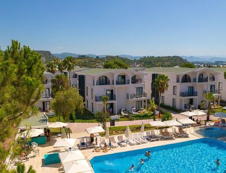 In einer begrünten Berglandschaft befinden sich eine weiße Hotelanlage mit Pool und mehreren Sportplätzen.
