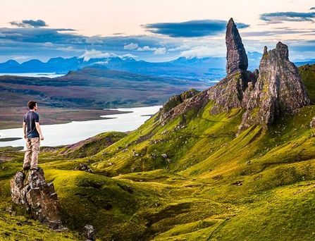 Reisetrends 2026: Eine grüne Berglandschaft mit bizarren Felsen und ein Mann steht auf einem Hügel