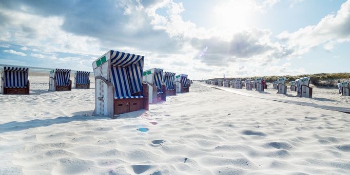 An einem weißsandigen Strand stehen viele weiß-blaue Strandkörbe.