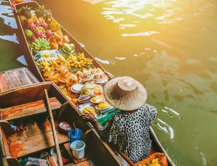 Eine asiatische Person mit Hut sitzt in einem Holzboot mit frischem Essen