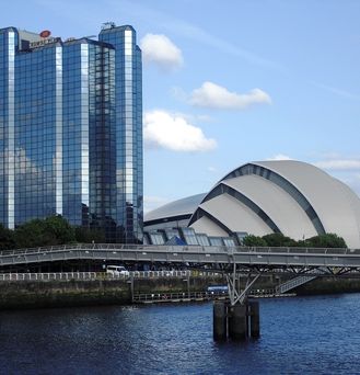 Ein moderne Hochhaus steht neben einem muschelförmigen Gebäude an einem Fluss. Eine moderne Brücke führt darüber.