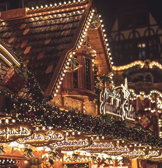 Eine weihnachtlich beleuchtete Fassade einer Holzhütte, die süße Leckereien anbietet