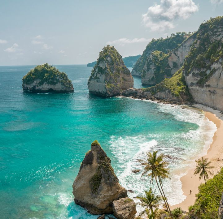 Strandurlaub Asien: Ein menschenleerer Strand mit tropischen Palmen zwischen Felsen