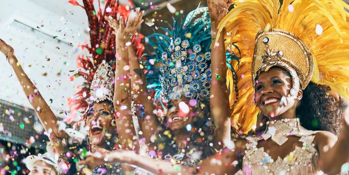 3 brasilianische Samba Tänzerinnen, mit traditionellem Kostüm stehen lachend nebeneinander und werfen glitzerndes Konfetti in die Luft.