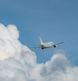 Ein weißes Flugzeug fliegt schräg durch den blauen Himmel über weißen puffrigen Wolken.