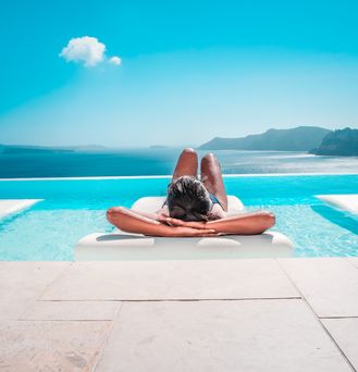Luxusurlaub: Eine Frau liegt auf einer Liege im Infinitypool mit Blick auf das Meer und die Berge