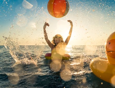 Ein Kind in einem Gummischwimmreifen spielt im Meer mit einem Ball.