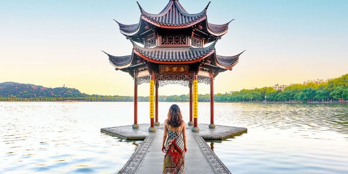 Am Ufer eines Flusses stehen mehrere goldene Buddah Statuen. Im Hintergrund Wolkenkratzer vor begrünten Flächen.