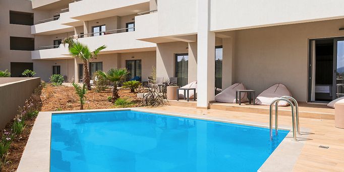 Direkt am Meer liegt eine Hotelanlage mit einer Poollandschaft zwischendrin immer wieder grüne Bäume und viele Sonnenschirme.