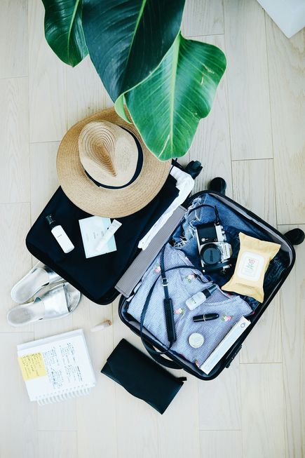 Ein geöffneter, vollgepackter Reisekoffer liegt auf dem Boden. Schuhe, eine Packliste und ein Sonnenhut liegen daneben.