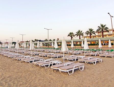 Um einen großen türkisen Pool stehen weiße mehrstöckige Häuser mit Palmen und Sonnenliegen davor.