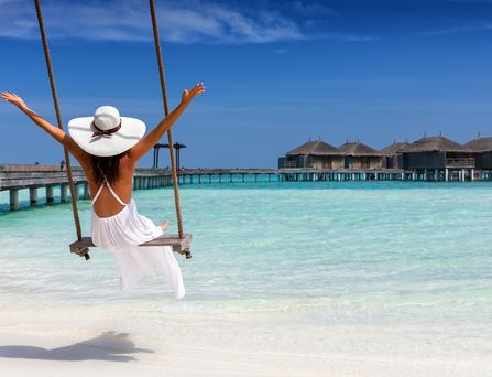 Dom Rep Urlaub: Eine Frau mit weiße Sommerkleid und Hut sitzt auf einer Schaukel am Strand.