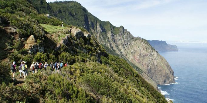 Eine Wandergruppe wandert durch eine begrünte Berglandschaft entlang der Küste.