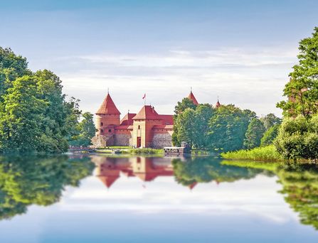 Blick von einem Felsenplateau auf einen tiefblauen Fjord, umgeben von bewaldeten Bergen unter blauem Himmel mit Wolken.