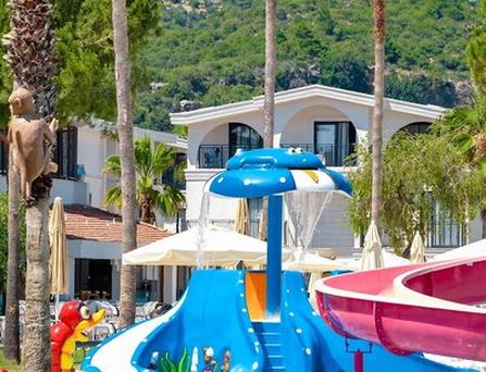 In einer begrünten Berglandschaft befinden sich eine weiße Hotelanlage mit Pool und mehreren Sportplätzen.