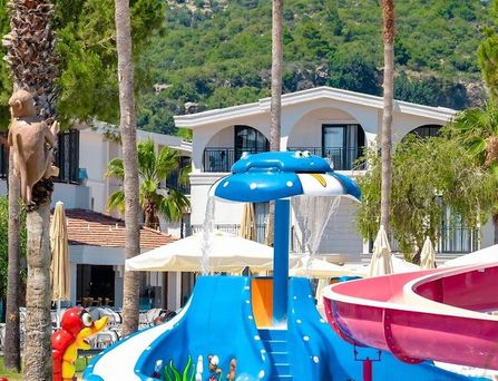 In einer begrünten Berglandschaft befinden sich eine weiße Hotelanlage mit Pool und mehreren Sportplätzen.