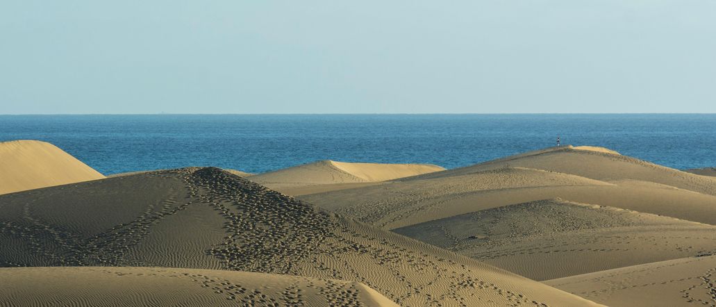 Eine bergige Wüste, im Hintergrund das tiefblaue Meer.