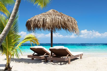 Urlaub in der Dom Rep: An einem weißen Strand stehen zwei Sonnenliegen mit Schirm.