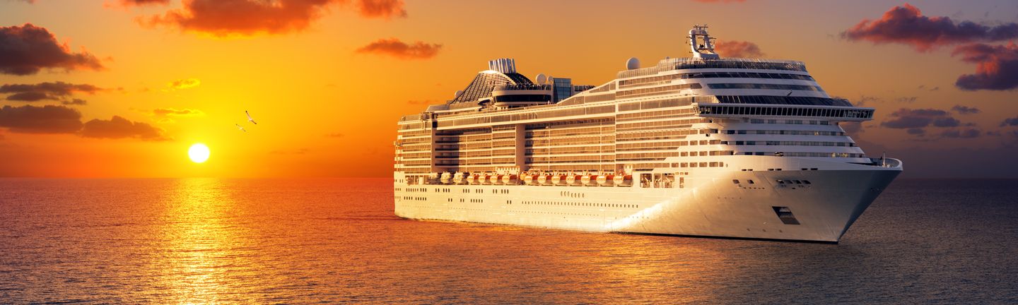 Die untergehende Sonne taucht die Szenerie in ein gold-orangenes Licht. Ein riesiges weißes Kreuzfahrtschiff gleitet auf dem glatten Meer.