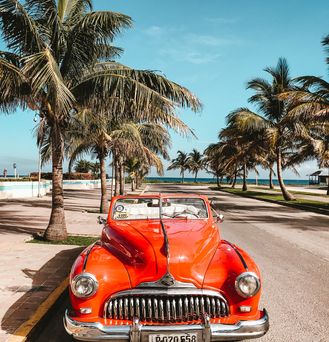 Auf einer Palmenallee nahe dem Strand steht ein knallroter Oldtimer.