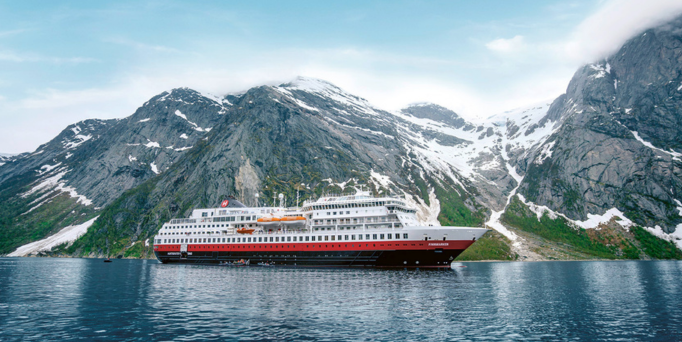 Großes Kreuzfahrtschiff auf ruhigem Meer vor einer Küstenstadt mit Hügeln im Hintergrund