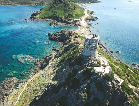Ein Felsen mit einer Steinruine ragt in das türkis-blaue Mittelmeer auf Korsika