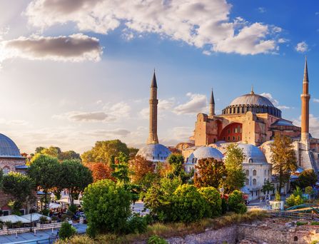 Sicht auf eine imposante, schöne Moschee, mit mehreren Kuppeln, welche aus einem bunt gefärbten Blätterdach emporragt.