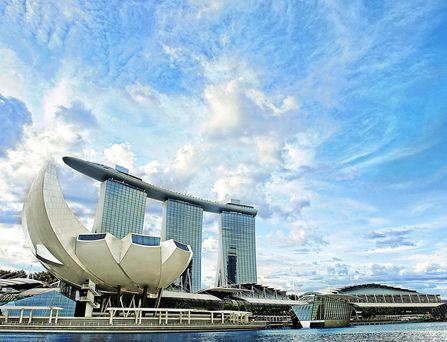 Am Ufer steht ein imposantes, 3-teiliges Gebäude und auf dem Dach dieser drei Gebäude liegt horizontal ein weiteres Gebäude. Das Hotel ist ein berühmtes 5-Sterne Haus in Singapur und repräsentiert die moderene Architektur.
