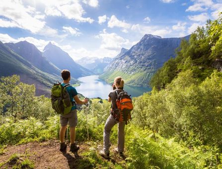 Zwei Wanderer stehen an einem Abhang und Blicken auf eine Bergwelt, durch die ein Fluss fließt
