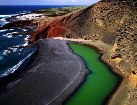 Ein schwarzer Strand an vulkanartigen Felsen mit einer giftgrünen Wasserlache