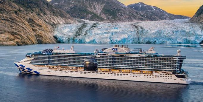 Großes Kreuzfahrtschiff mit mehreren Decks fährt auf ruhigem Wasser vor Gletscher und Bergen bei Sonnenuntergang.