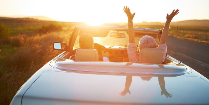 Ein Paar fährt in einem Oldtimer Cabrio der Sonne entgegen.
