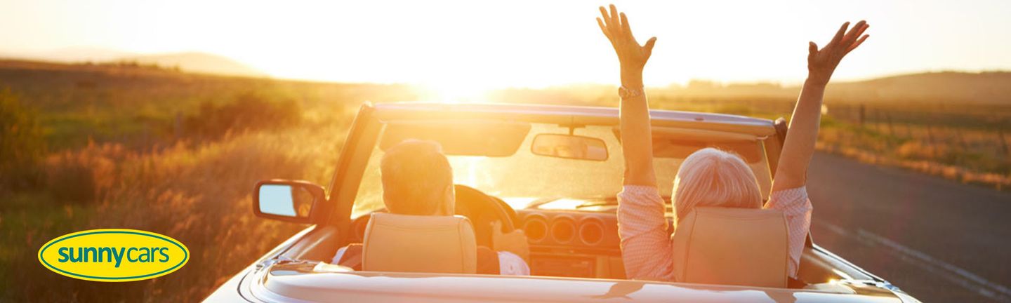 Ein Paar fährt in einem Oldtimer Cabrio der Sonne entgegen.