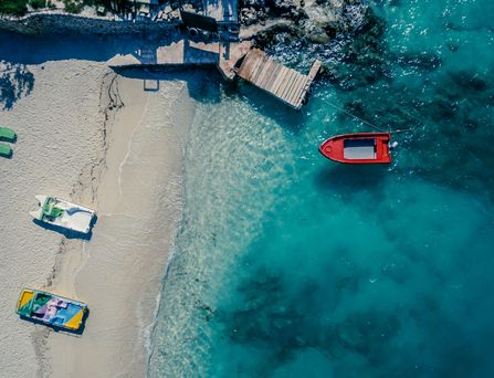 Eine Luftaufnahme von einem weißen Sandstrand mit Booten an türkis-blauem Wasser.