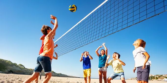 Unter knallblauem Himmel spielen 6 Kinder Volleyball am Strand.