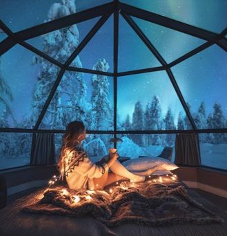 Eine Frau mit Norwegerpulli sitzt unter einer Glaskuppel in einer verschneiten Landschaft.