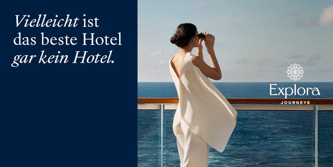 Großes Kreuzfahrtschiff auf ruhigem Meer vor einer Küstenstadt mit Hügeln im Hintergrund