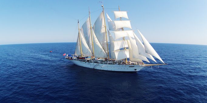 Ein riesiges Segelschiff mit weißen Segeln gleitet auf dem tiefblauen Meer dahin.