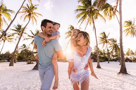 Urlaub in der Dom Rep: An einem weißen Strand läuft eine glückliche Familie durch Palmen.