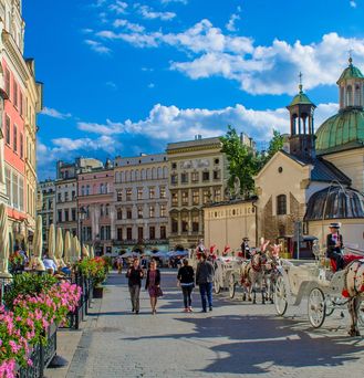 Ein historischer Altstadtkern im Frühjahr oder Sommer: Alles blüht, barocke Häuserfassaden und eine Kutsche fährt auf Kopfsteinpflaster.