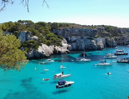 Eine steinige, steile Bucht mit vielen Seegelbooten auf türkisem Wasser.