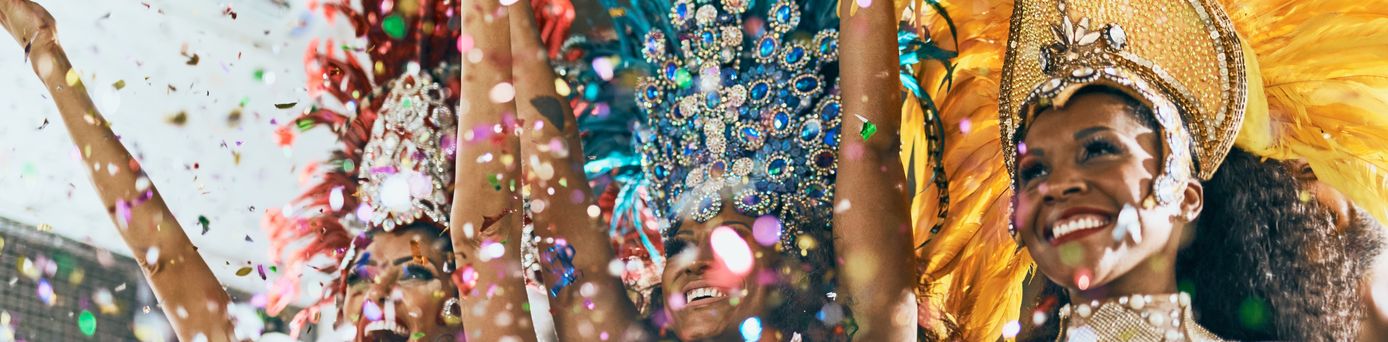 3 brasilianische Samba Tänzerinnen, mit traditionellem Kostüm stehen lachend nebeneinander und werfen glitzerndes Konfetti in die Luft.