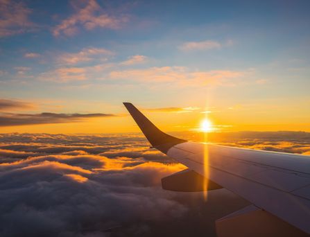 Blick aus einem Flugzeugfenster auf den Flügel über den Wolken und die Sonne am Himmel
