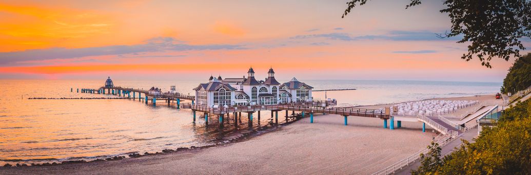 Am Strand mit orange-rosanem Sonnenuntergang ragt die Seebrücke Sellin ins Meer rein.