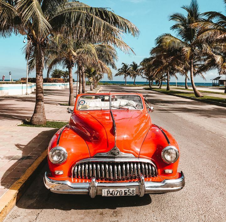 Auf einer Palmenallee nahe dem Strand steht ein knallroter Oldtimer.