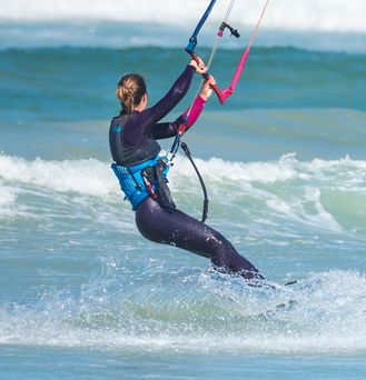 Eine Frau hält die Kiteausrüstung in den Händen und steht im grün-blauen Wasser.