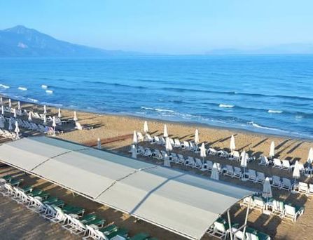 Um einen großen türkisen Pool stehen weiße mehrstöckige Häuser mit Palmen und Sonnenliegen davor.