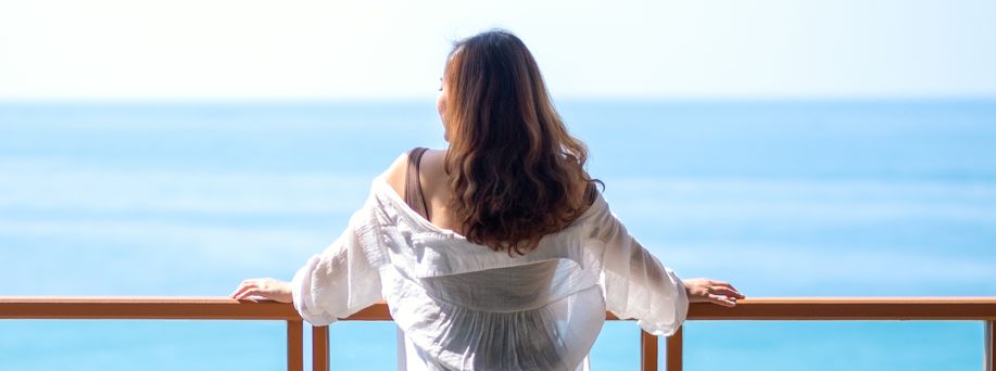 Eine Frau mit weißer Bluse steht an einem Geländer eines Schiffes und blickt auf die offene See.